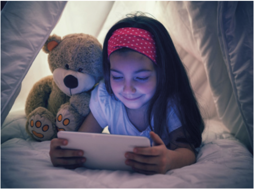 Niña usando una tablet bajo las sábanas en la oscuridad